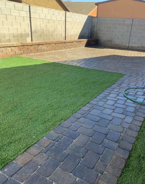 Synthetic grass turf surrounded by brick patio within the backyard.