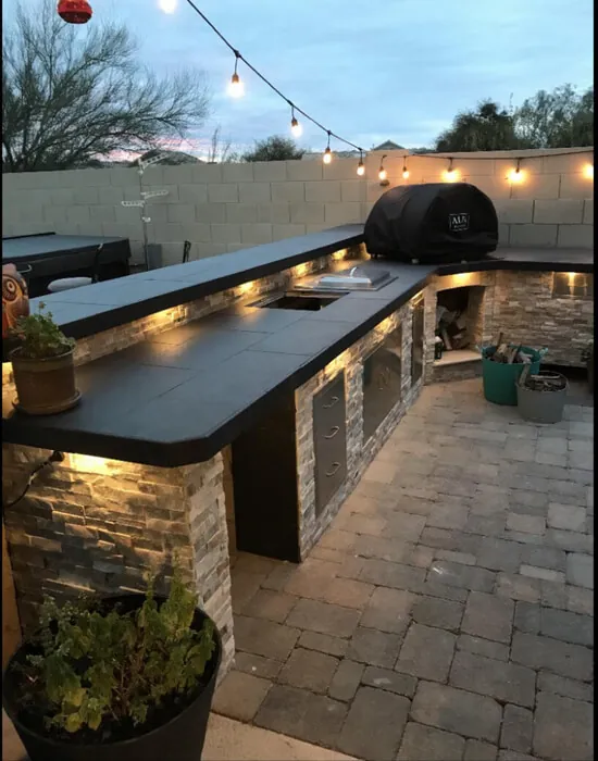 Backyard with custom bbq builds including tiled countertop, cabinets, lights, and an outdoor wood-fired oven.