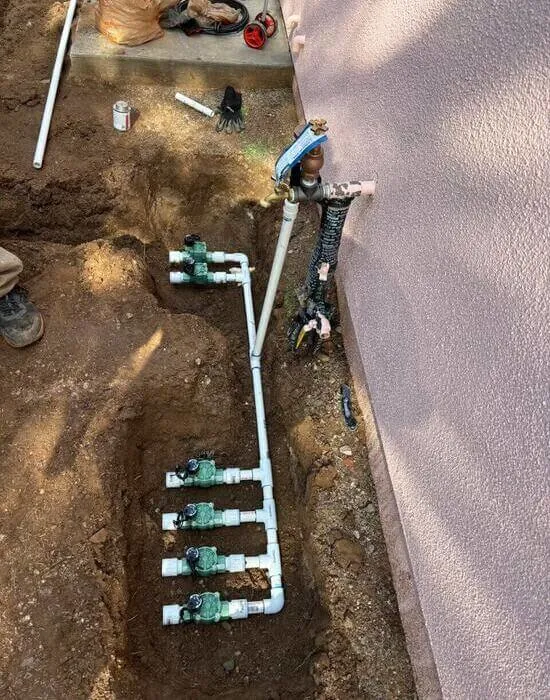 An exposed pipe emerging from a wall and branching into multiple lines. Used as part of an irrigation diagnostic.