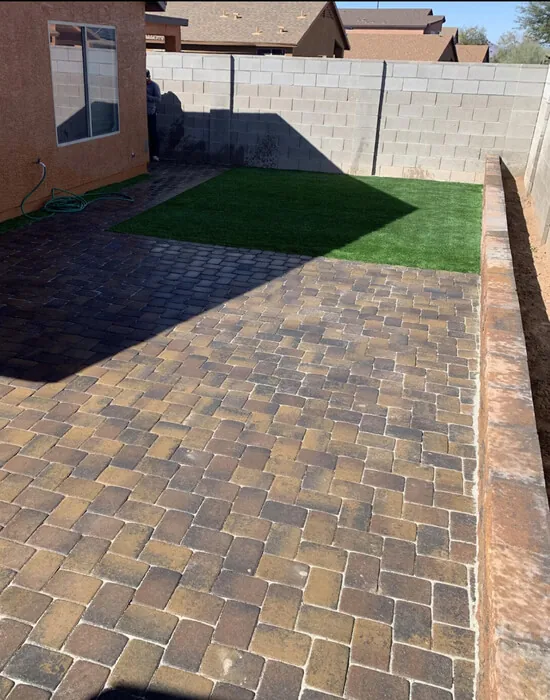 A backyard view with a hardscaping, tiled patio that surrounds most of the backyard and a small grass patch in the corner of the backyard.