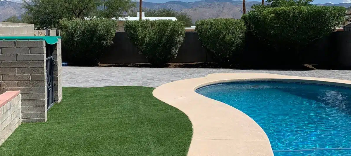 A backyard featuring a spacious pool on one side, artificial turf on the other, and paved tiles lining the rear of the yard, an example about Alpha Team Landscaping and their services.